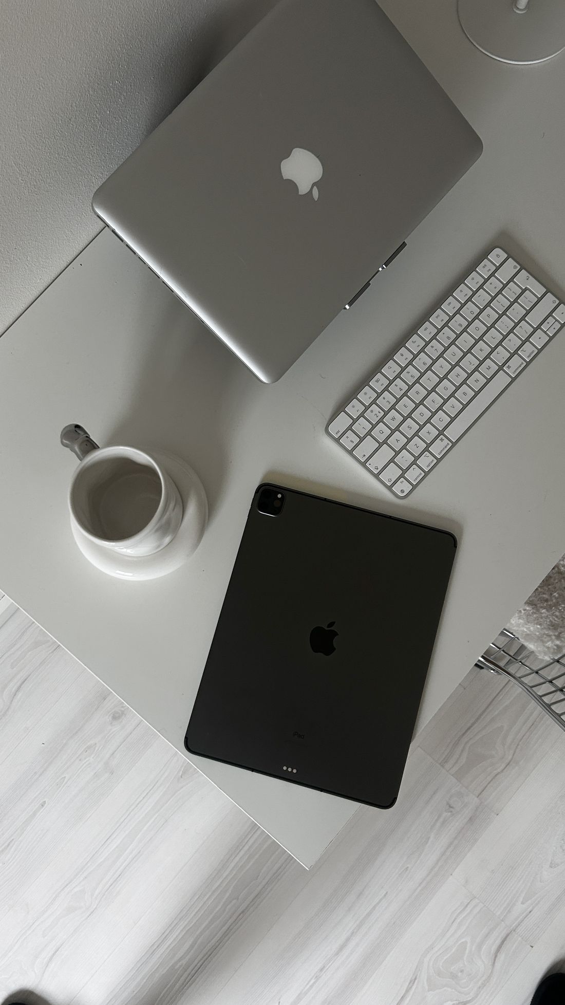 Laptop, tablet, keyboard and coffee laid out on a white desk